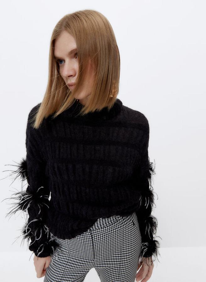 En punto elástico y color negro, con cuello semicisne y mangas largas con apliques de plumas este jersey con acabados en rib podemos encontrarlo en las tallas S y M por 99 euros.