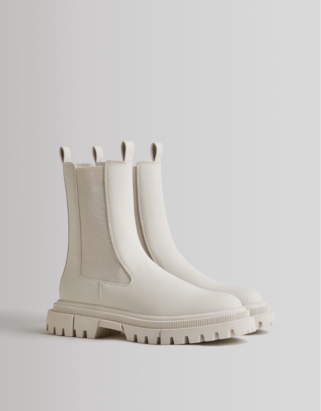 En color beige, con suela track y trabillas frontal y trasera, estos botines engomados de Bershka con elásticos tobilleros cuestan 35,99 euros y están disponibles entre los números 35 y 41.