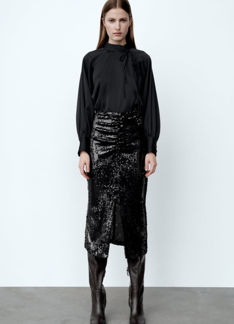 Imagen - Con blusa de lazada al cuello, botas altas y falda de lentejuelas.