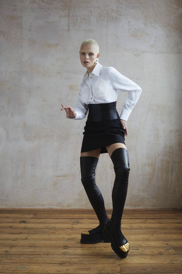 Camisa con aplicaciones, minifalda, botas altas y pendientes, todo de Schiaparelli.