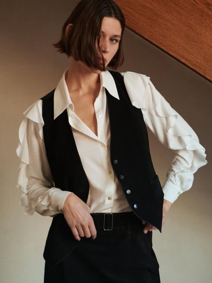 Las blusas blancas serán tus mejores aliadas para los looks de oficina de los próximos meses. Si quieres darle un aire nuevo a esta clásica prenda, añade un chaleco de color negro. Blusa con volantes de Massimo Dutti (49,99 euros). 