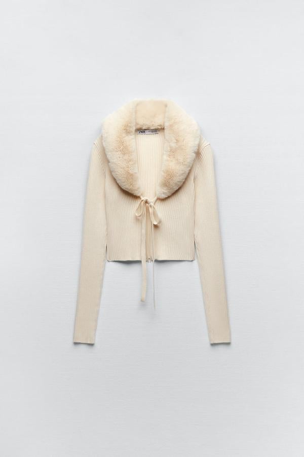 Una chaqueta de punto que no es como todas las demás. En color blanco y con un elegante cuello de pelo. Cárdigan corto de punto de Zara (25,99 euros). 