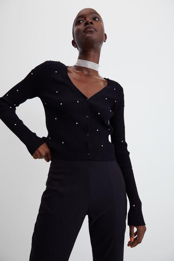 En color negro, con strass brillante salpicando toda la prenda, este cárdigan corto en punto de canalé de que solo podemos encontrar en la tienda online de H&M viene con escote de pico y botonadura frontal y cuesta 24,99 euros. 