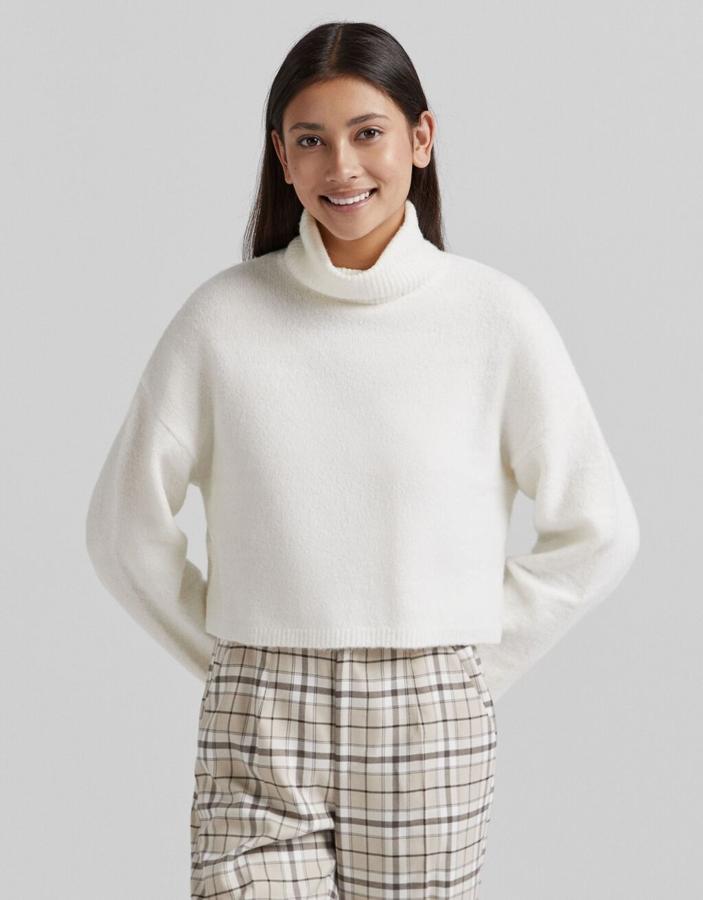 Diseño cropped para este jersey de punto de Bershka disponible en lila, gris y crudo que viene con diseño de hombros caídos y cuello alto. Tiene un precio de 19,99 euros. 