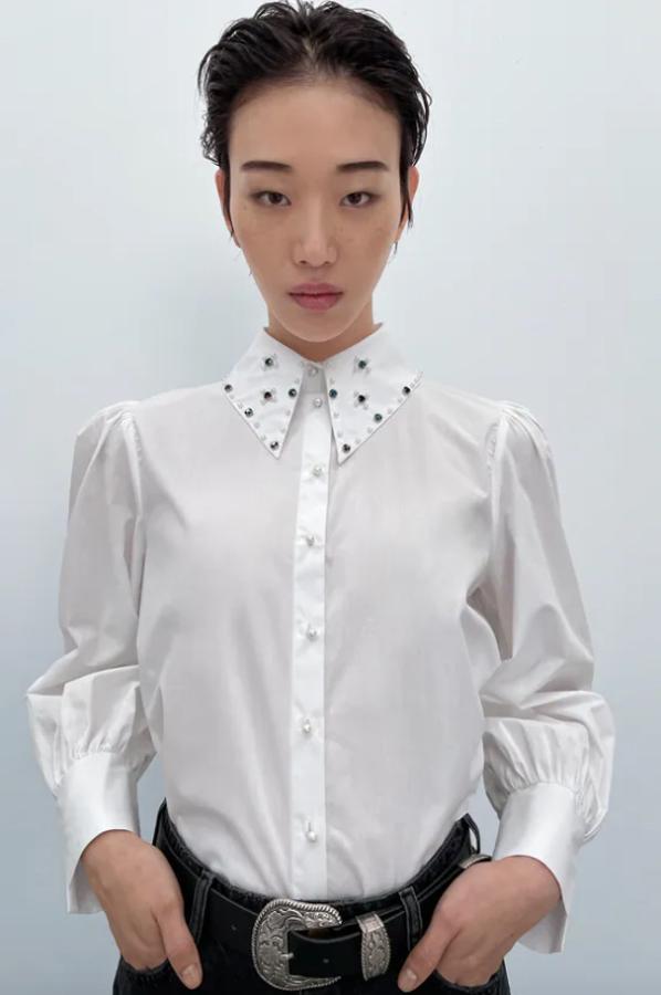 Aplicación de abalorios en el cuello de solapa para esta camisa blanca de Zara con mangas largas acabadas en abertura y cierre frontal de botones en perla que cuesta 25,95 euros. 