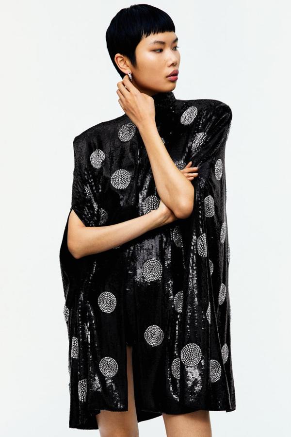 Majestuosa capa en tejido de lentejuelas de poliéster reciclado, embellecida con strass parcialmente elaborado con vidrio reciclado. Modelo con sisas caídas y cuello alto con cierre de corchete oculto (249 euros).