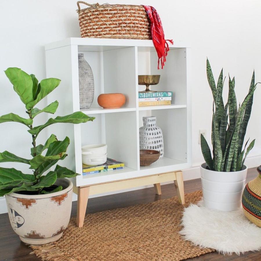 La estantería cuadrada de cuatro módulos de la serie Kallax puede parecer muy sosa, pero si le incluyes unas patas de madera, el resultado es espectacular.