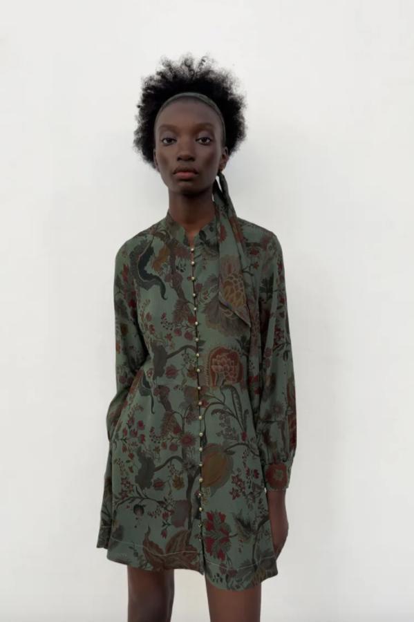 Cuello redondo subido y cierre de botones dorados frontal para este vestido mini de Zara en verde grisáceo con un precioso estampado de flores granates que viene con cinturón lazada en el mismo tejido. Cuesta de 39,95 euros. 