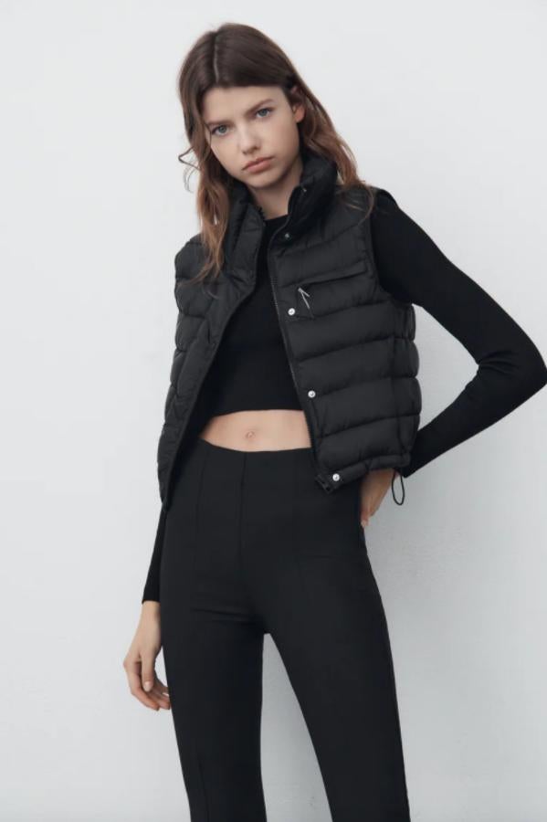 Diseño corto para este chaleco negro confeccionado en tejido water repelent y acolchado. Tiene bolsillo frontal con cremallera, bajo ajustable con cordones elásticos y un precio de 25,95 euros. 