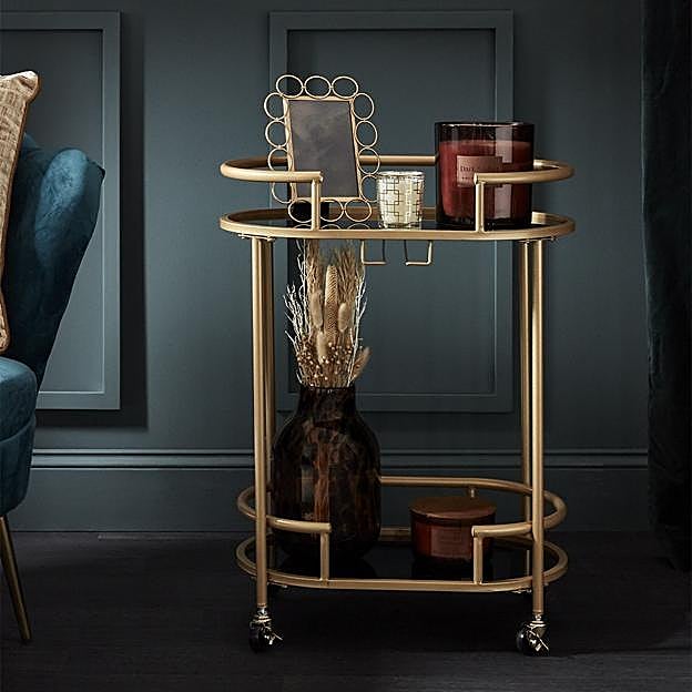 Imagen principal - La camarera dorada cuesta 35 euros en Primark Home, el mueble de ratán cuesta 60 euros y la estantería de baño, 30 euros. 