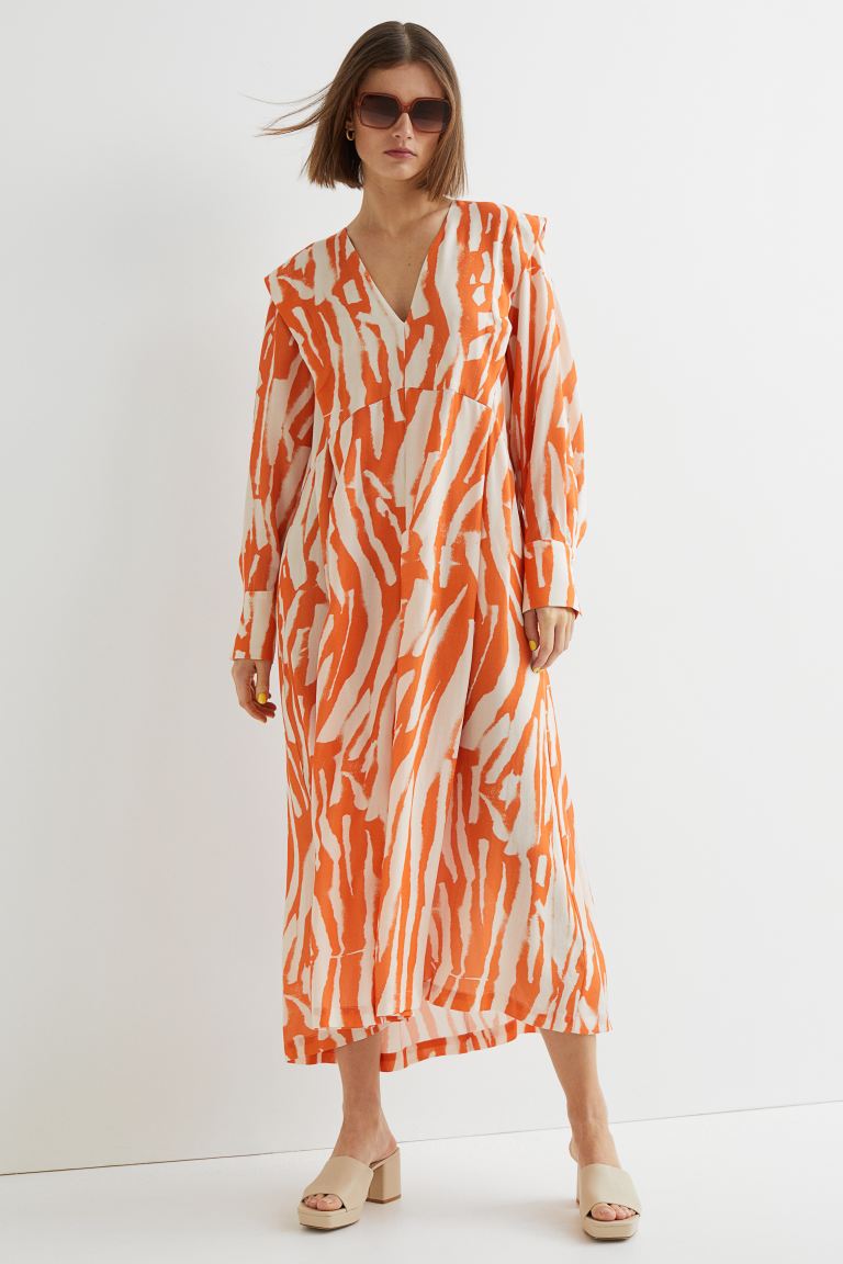 Con hombros marcados y puños abotonados, este vestido estampado de H&M en blanco y naranja que solo podemos comprar en la web de la firma es de diseño tobillero y tiene la falda con ligero vuelo y las mangas largas con puños abotonados. De corte asimétrico a la cintura, falda con pliegues y diseño de hombros marcados, está confeccionado en lyocell y tiene un precio de 49,99 euros. Está disponible entre las tallas XS y XXL.