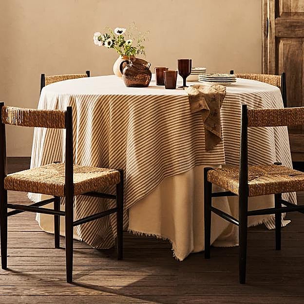 Imagen principal - El mantel de lino con estampado de rayas en tonos tierra cuesta 25.99 euros en Zara Home. La vajilla de loza pintada, desde 4.99 euros la pieza, el mismo precio de las servilletas bordadas personalizadas.