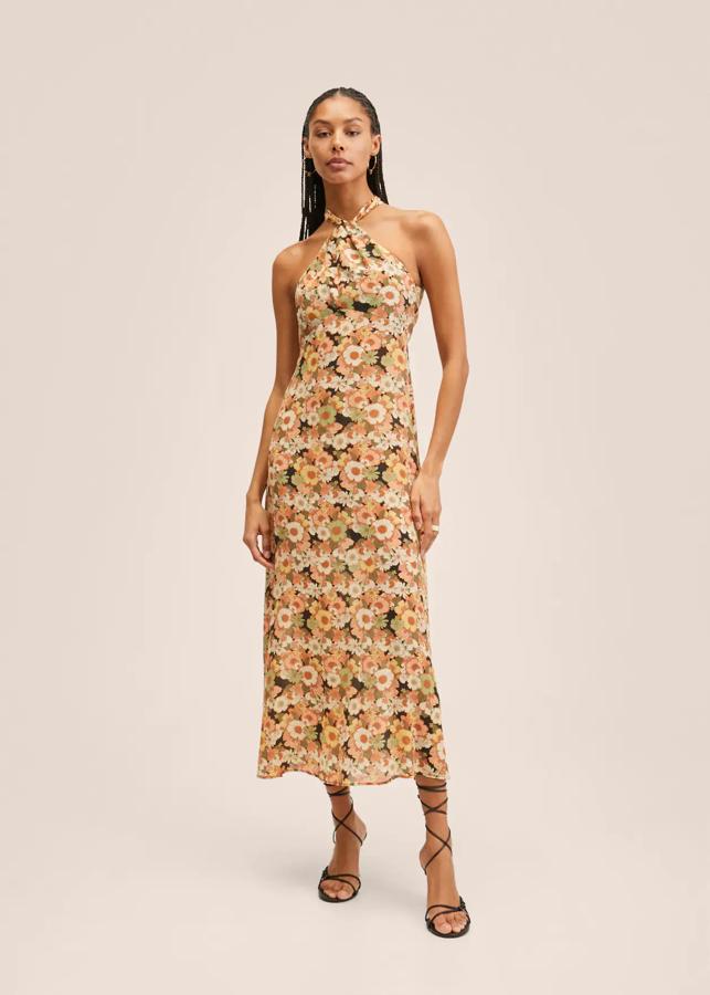 Uno de nuestros diseños favoritos es este precioso vestido con estampado de flores en tonos salmón, verdes y amarillos sobre fondo negro de Mango. Confeccionado en tejido fluido, de diseño largo evasé y con cuello halter, viene con nudo frontal y cierre de cremallera en la parte posterior. Podemos comprarlo por 49,99 euros. 