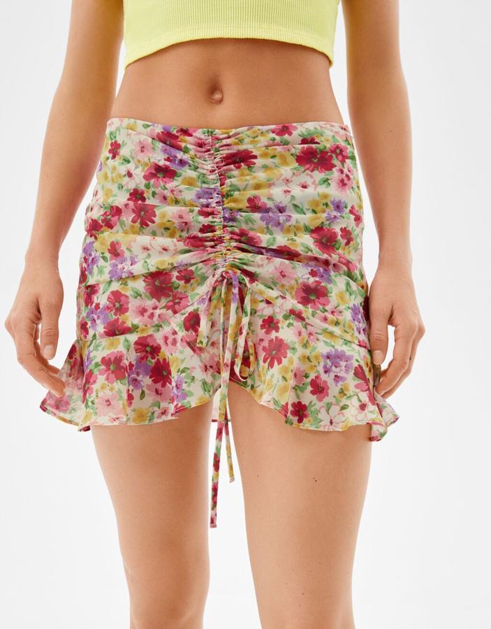Fruncido frontal y volantes para esta minifalda de Bershka con estampado de flores en tonos rojos, rosas y lilas sobre fondo blanco. Tiene un precio de 17,99 euros. 
