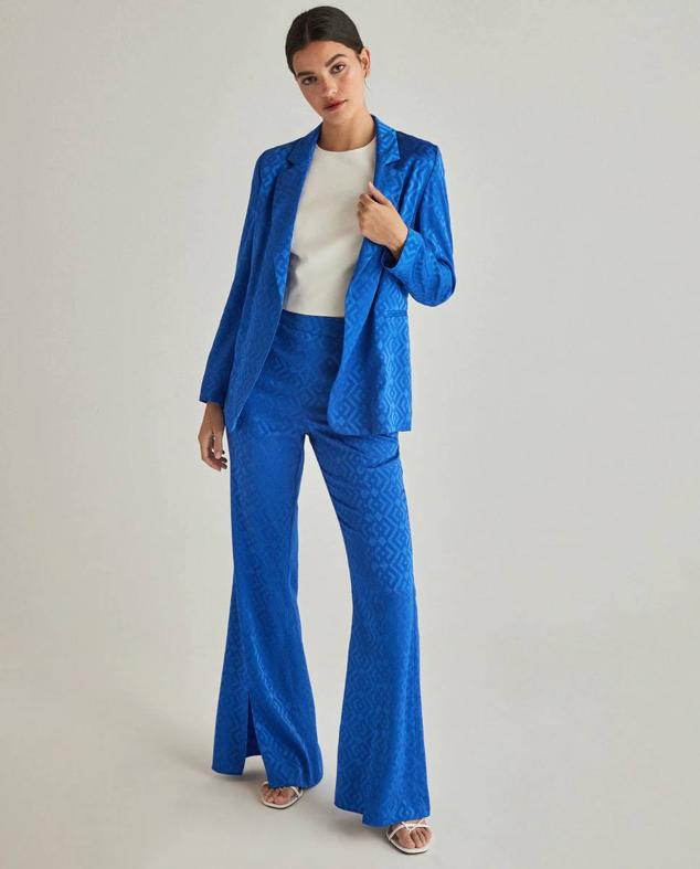 Traje de Green Coast con estampado geométrico a tono color azulón. Se basa en dos piezas, una blazer con cuello solapa y diseño abierto con un precio de 49,99 euros y un pantalón de campana en el mismo estampado y tejido, también por 49,99 euros. Está disponible en El Corte Inglés.