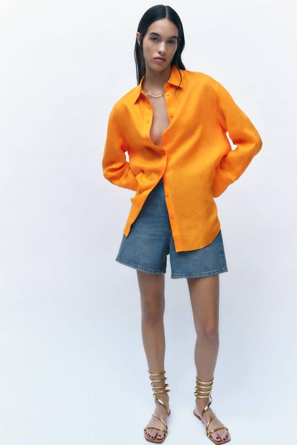 Camisa amplia confeccionada en tejido de lino, con cuello solapa, manga larga acabada en puño, bajo asimétrico y cierre de botones a tono, color naranja, de Zara. La encontrarás por 29,95 euros.