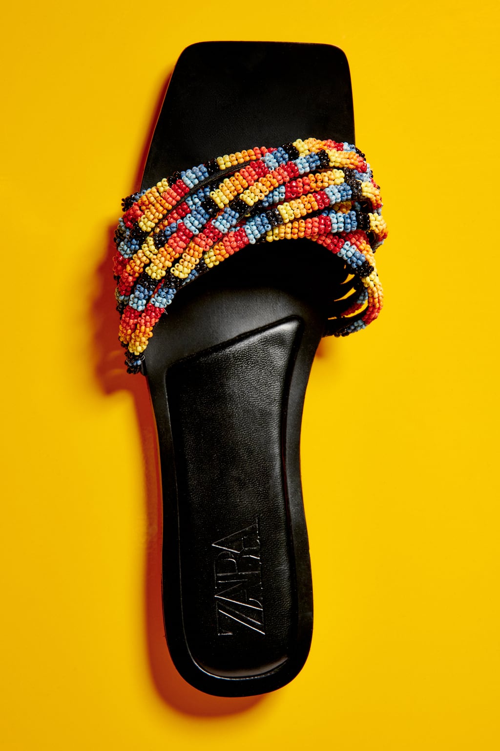 Un diseño con aires étnicos que combina el negro con dos tiras de abalorios de colores. Sandalias planas de Zara (35,99 euros) 