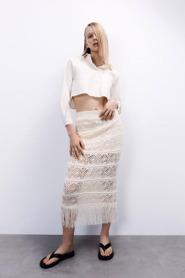 Falda midi confeccionada en tejido de punto calado, con talle alto, silueta acomodada a la figura y bajo acabado en flecos, tono crema. La encontrarás en las tallas S, M y L a 29,99 euros.