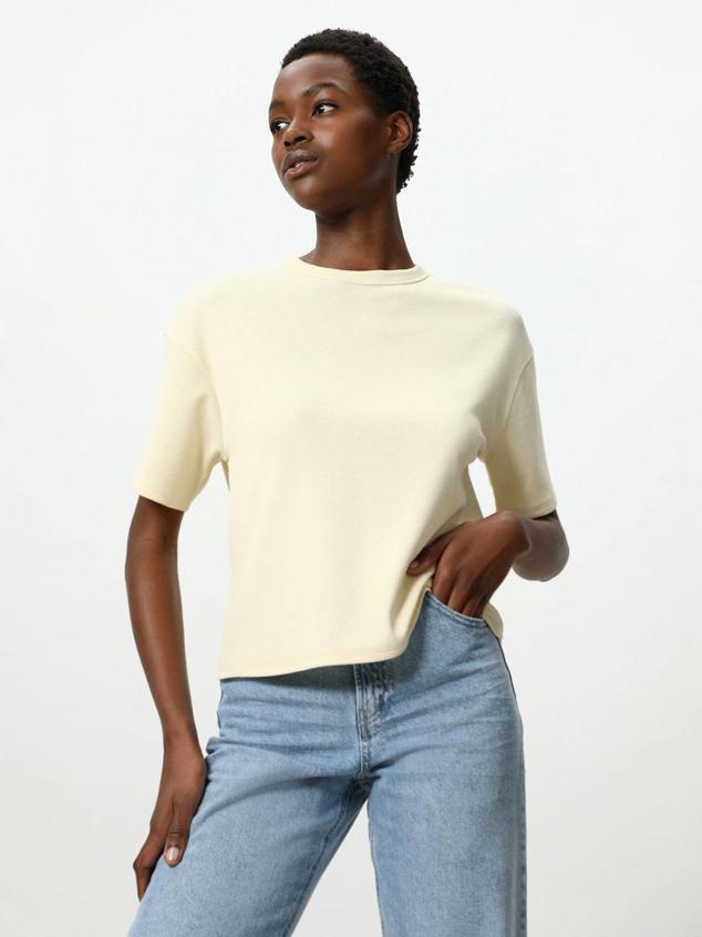 Camiseta oversize en tejido con textura, de manga corta, cuello redondo y detalle de nudo y abertura en la espalda. La encontrarás en vainilla, blanco, arcilla, verde agua y rosa claro, a 7,99 euros.