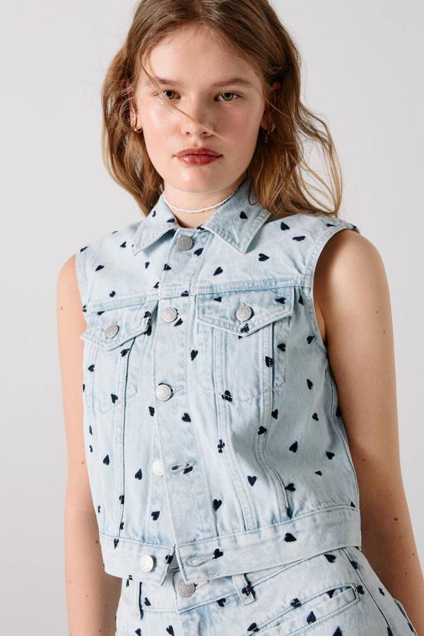 Chaleco en tejido denim estilo retro con manga sisa, cuello solapa, bolsillos en el pecho, cierre de botones y detalles bordados de corazones, en azul medio. Cuesta 69,99 euros.