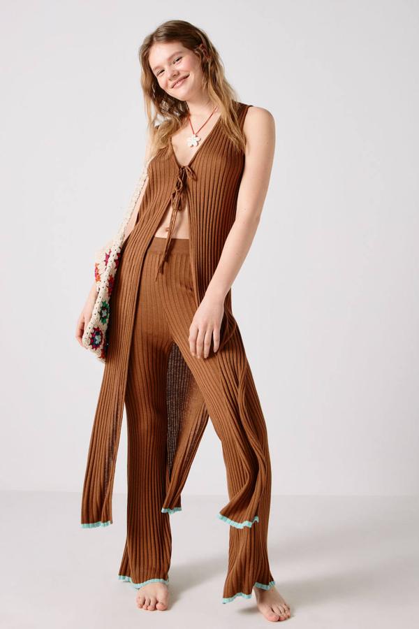 Chaleco largo en tejido de punto canalé con escote en uve, cierre mediante lazada, aberturas y ribete a contraste en el bajo, color marrón oscuro. Tiene un coste de 59,99 euros.