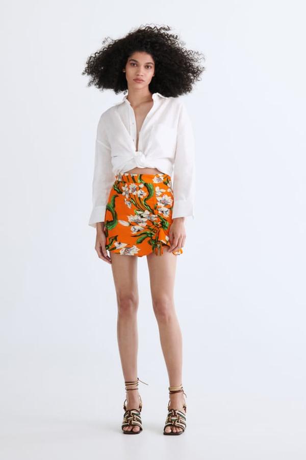Falda pantalón de tiro alto con frunces delanteros cordones. Bajo acabado en volante y estampado floral en el que predominan los tonos naranjas. Precio: 25,95 euros.