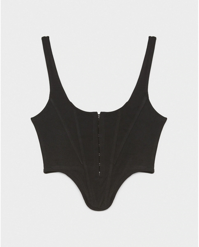 De corte asimétrico y totalmente negro. Este es el corsé más ponible y versátil que tiene El Corte Inglés. Podrás combinarlo con todo tu armario sin ningún problema. Precio: 13,99 €.