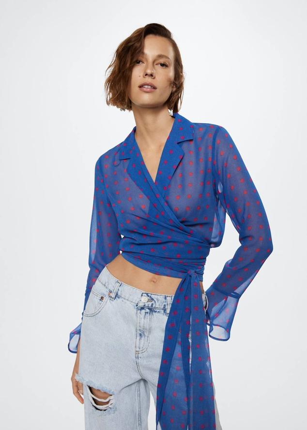 Blusa confeccionada en tejido ligero semitransparentes con estampado de lunares azul y rojo, cuello solapa con muesco, manga larga terminada en volante y cierre de lazada, de Mango. Puedes comprarla por 29,99 euros.