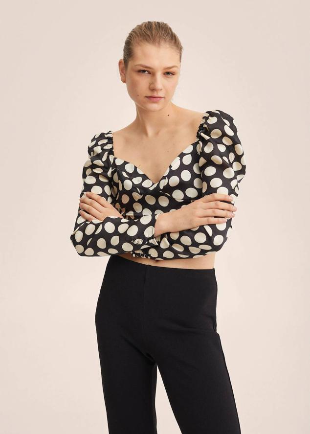 Blusa cropped en tejido satinado con estampado de lunares grandes en blanco y negro. Tiene manga larga abullonada, escote corazón y detalle de elástico tipo nido de abeja en la espalda, de Mango. La encontrarás rebajada de 25,99 euros a 17,99 euros.