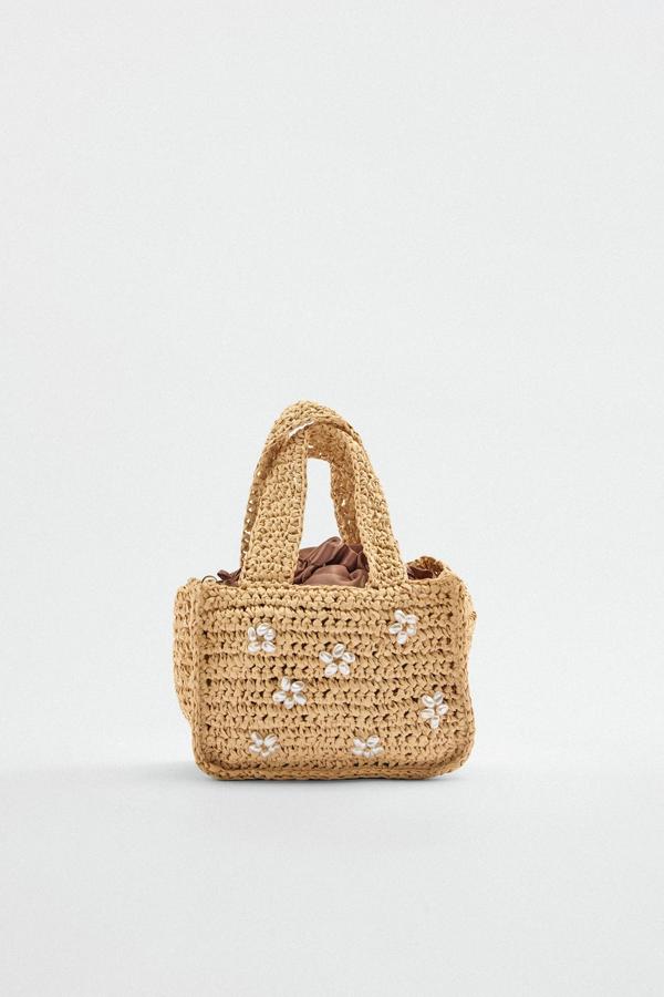Unos pequeños detalles, como unas flores formadas por cuentas de perlas, son más que sufcientes para convertir un simple bolso de rafia en una pieza especial de tu armario. Bolso de mano de Zara (22,99 euros) 