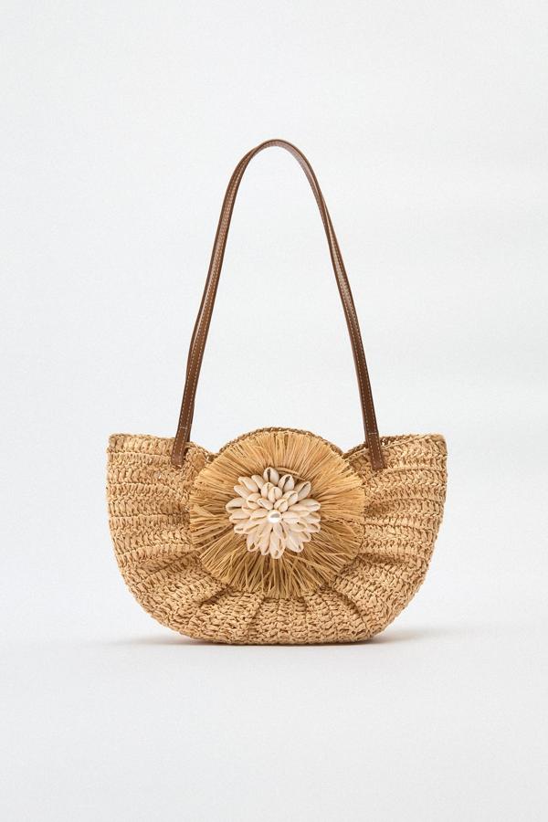 El bolso más original del verano acaba de llegar a Zara, Un diseño insipirado en los capazos playeros pero repleto de detalles. Sus asas largas de cuero hacen que lo puedas llevar en cualquier momento. Bolso con flor de rafia de Zara (29,99 euros)