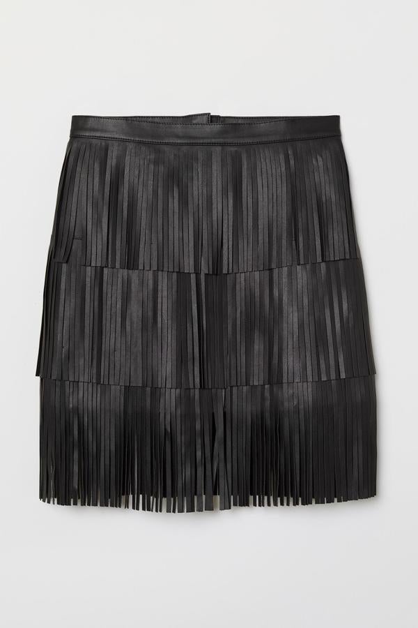 Falda corta negra en piel sintética con hileras de flecos. Se trata de un modelo de talle alto con cremallera oculta y cierre de corchete detrás, además no tiene forro. Es de H&M. Precio: 44,99 €.