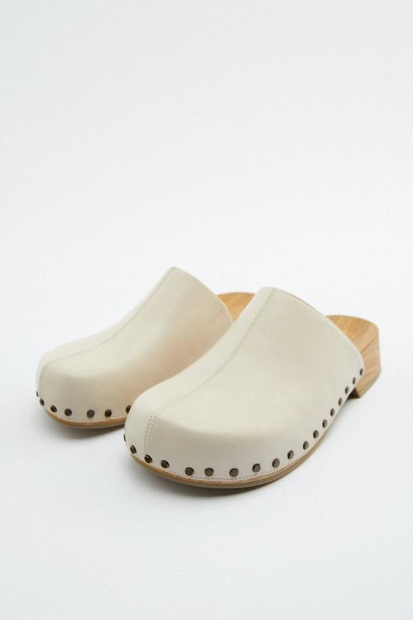 Zueco en color blanco con detalle de tacha. Posee un detalle con aplique metálico. También tiene una suela de madera de 4 cm. Es de Zara. Precio rebajado: 19,99 €. 