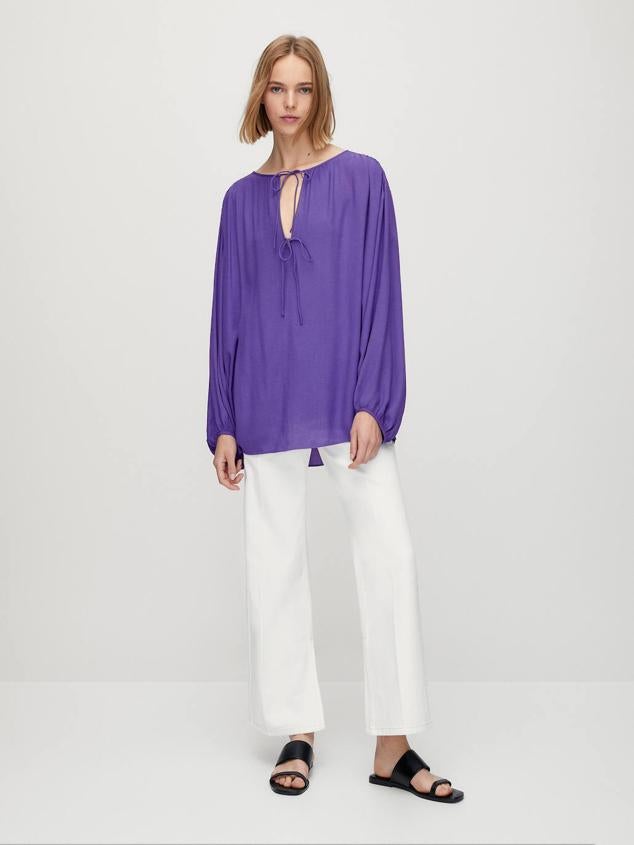 Blusa fluida de silueta holgada y relajada, cuello redondo, cierre de lazadas a tono y manga larga ligeramente abombada, color morado. Tiene un coste de 25,95 euros, con descuento.