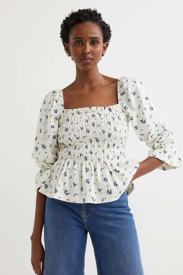 Top fruncido de manga larga, con escote cuadrado tipo top y mangas abullonadas. Es 100 % algodón, con un material que destaca por ser cada vez más sostenible al ser en parte reciclado. El estampado floral es precioso, en color blanco natural y las flores en azul. Es de H&M. Precio: 14,99 €.