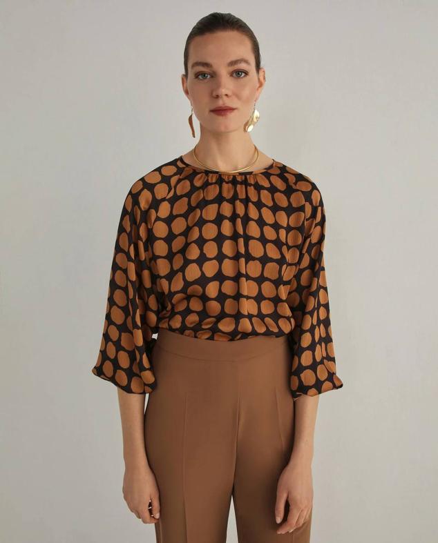 Blusa fluida con cuello redondo, manga por debajo del codo amplia y estampado de lunares en marrón y negro, de Woman El Corte Inglés. La encontrarás con descuento a 19,99 euros.