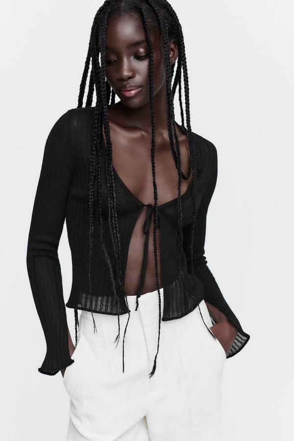 Chaqueta de punto semitransparente con diseño acanalado, escote de pico, manga larga acabada en abertura y cierre mediante lazada, en negro, de Zara. Tiene un precio de 22,95 euros.