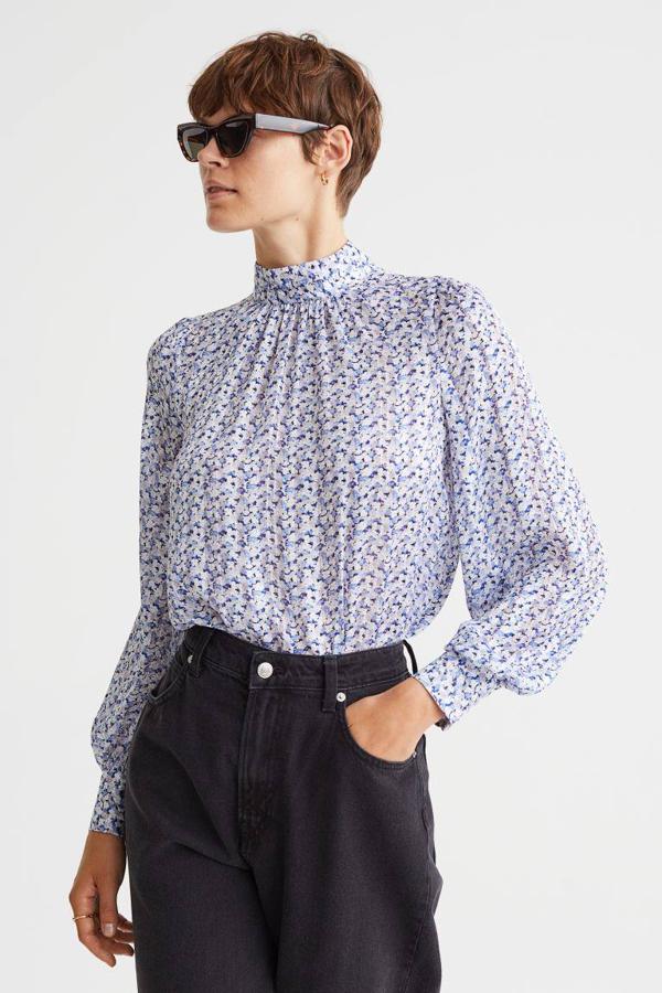 Esta blusa de color azul tiene el cuello elevado, mangas globo y una abertura en la espalda.