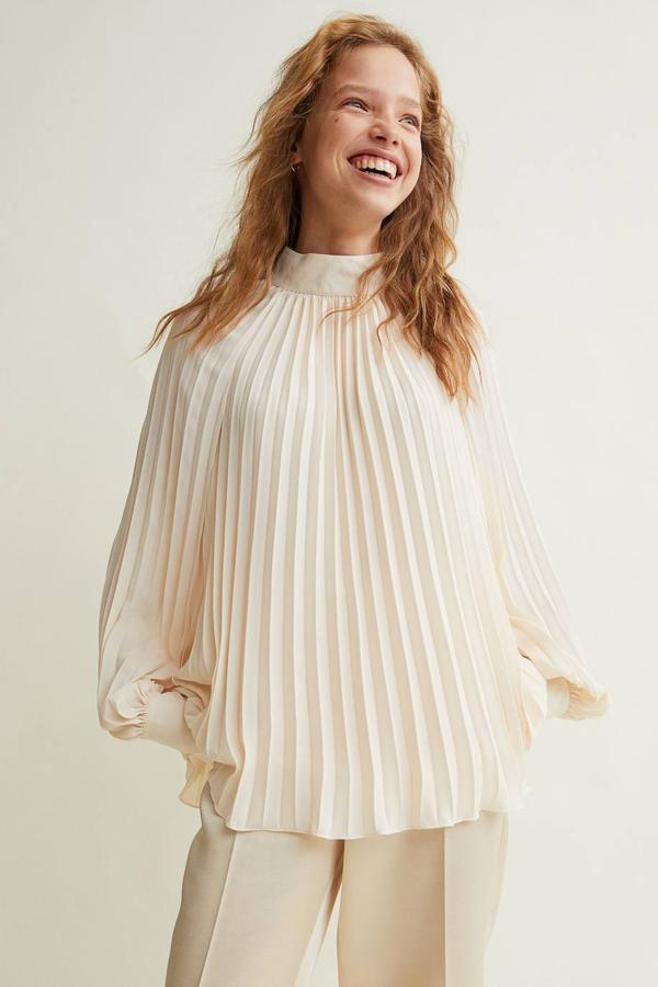 Blusa en tejido plisado con cuello elevado, mangas globo largas de corte raglán y puños anchos, color crema, de H&M. Cuesta 29,99 euros.