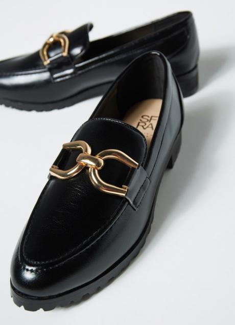 Imagen - Los mocasines son negros y tienen un detalle dorado.