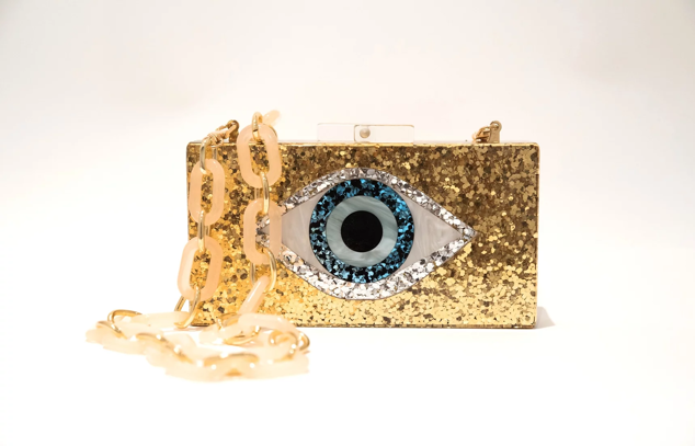 Bolso dorado con detalle de ojo central a modo detalle. Cuenta con lentejuelas de diferentes colores muy sutiles para looks elegantes y formales. Confeccionado con cadena de metal oro y acrílico nude. Es de Hobe. Precio: 84 €.