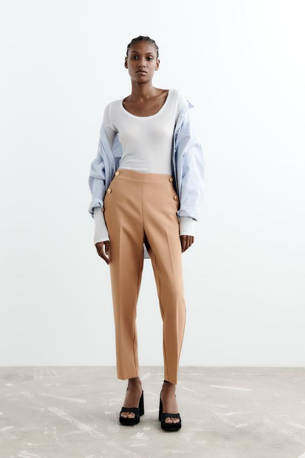 Un pantalón de vestir diferente a todo lo que tienes en tu armario. Pantalón color arena con doble botonadura dorada de Zara (27,99 euros). 
