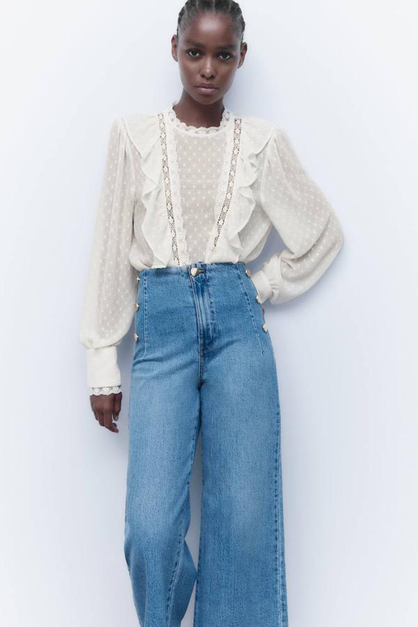 Blusa de plumeti con cuello redondo, manga larga ligeramente abullonada acabada en puños anchos, cuerpo fluido, detalles bordados y volantes, en crudo, de Zara. La encontrarás por 25,95 euros.
