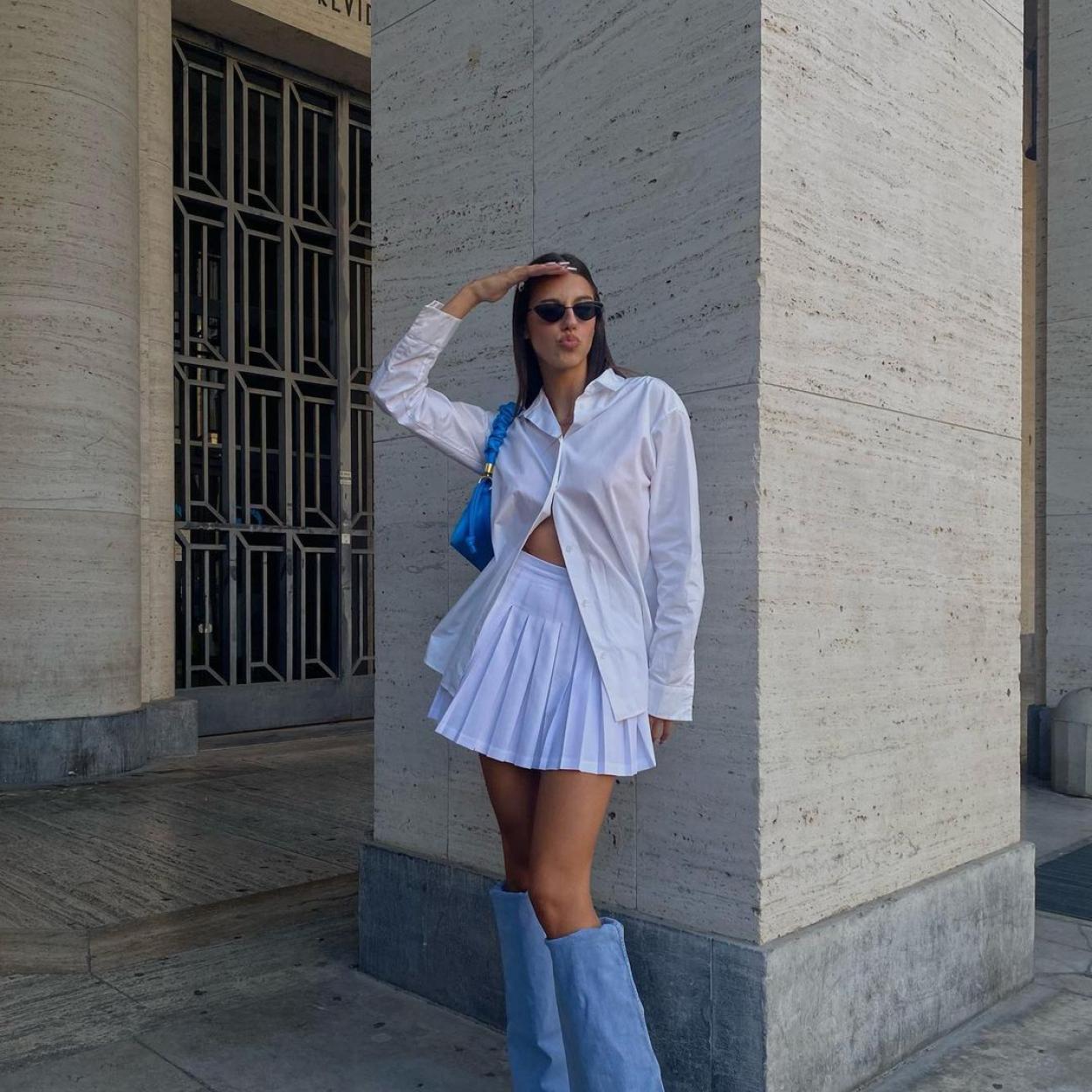 La influencer lleva una minifalda plisada con una camisa blanca que combina con unas botas altas de color azul. 