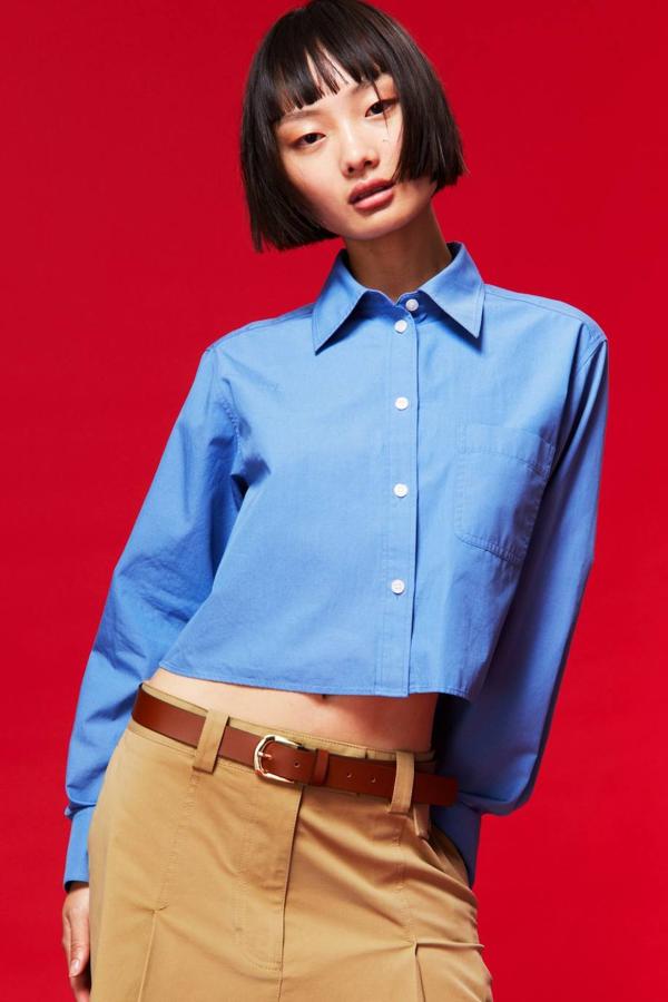 Camisa cropped de popelín con efecto frufrú, cuello solapa, cierre de botones, manga larga recogida en puño ancho y bolsillo en el pecho, color azul, de H&M. Cuesta 22,99 euros.