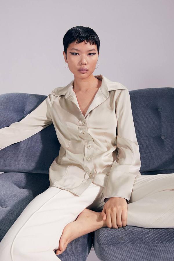 Camisa en tejido fluido satinado con corte entallado, cuello solapa de pico, manga larga con puños anchos, bajo asimétrico y cierre de botones, en tono beige claro, de H&M. La encontrarás por 24,99 euros.