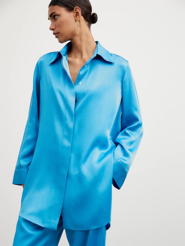 Camisa larga fluida en tejido satinado con cuello solapa, manga larga ancha y cierre de botones oculto por tapeta, color turquesa, de Massimo Dutti. Puedes comprarla a 79,95 euros.