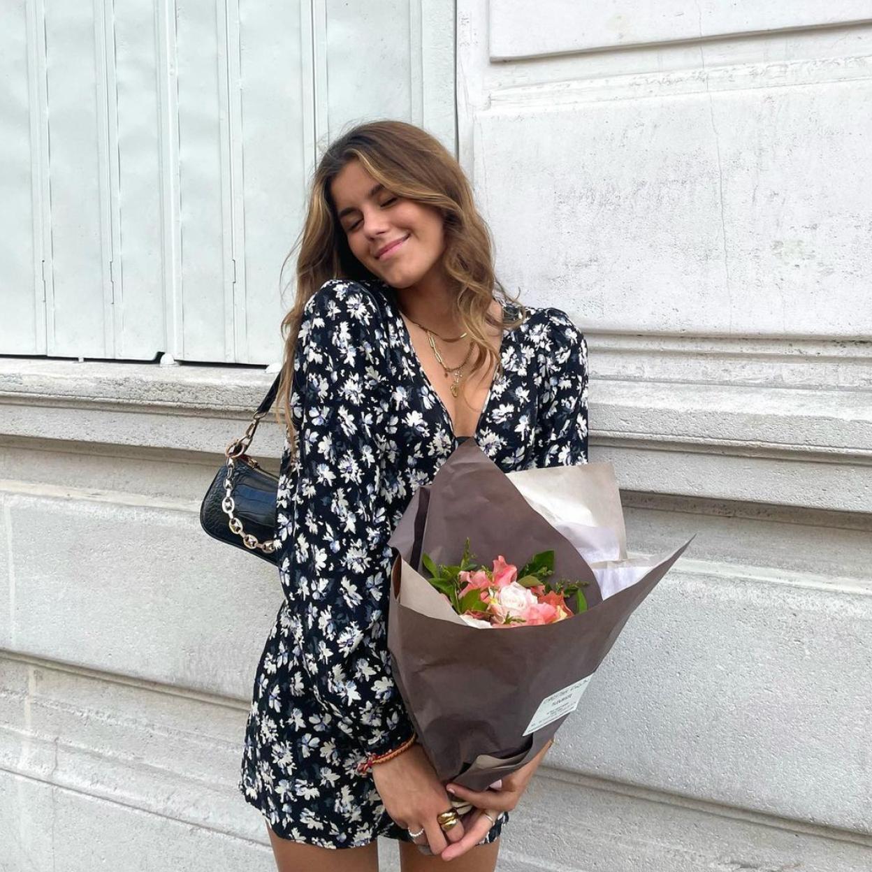 La influencer lleva un vestido estampado de manga larga y carga un ramo de flores. 
