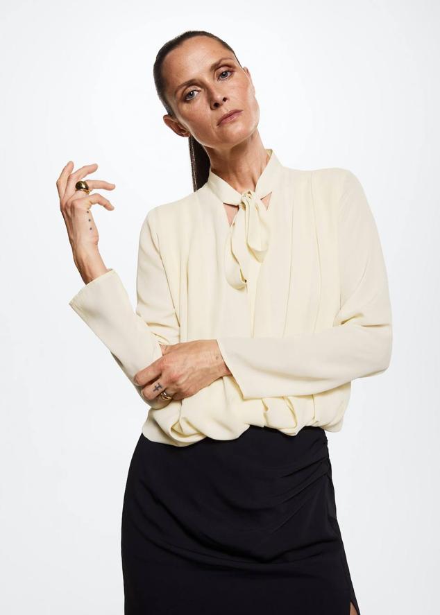 Blusa fluida con detalles plisados, diseño cruzado, manga larga y lazada al cuello, en tono blanco roto, de Mango. Está disponible por 29,99 euros.