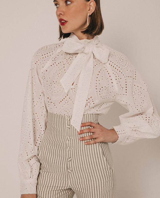 Camisa romántica en tejido perforado con manga larga abombada y cuello subido con lazada, en blanco, de Cherubina. La encontrarás en El Corte Inglés por 52 euros.